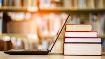 An open laptop sitting on a table, next to a collection of 4 stacked books.