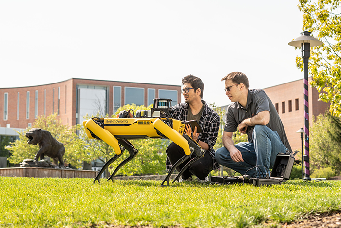 Two people squatting down next to a robotic dog.