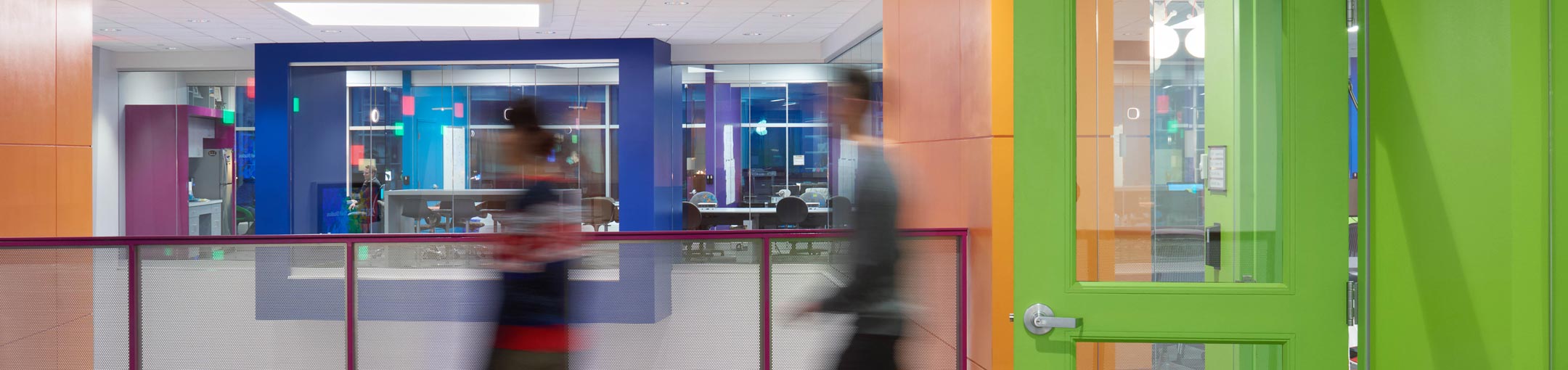 a motion blurred photo of two people walking through the color hallways of the MAGIC center