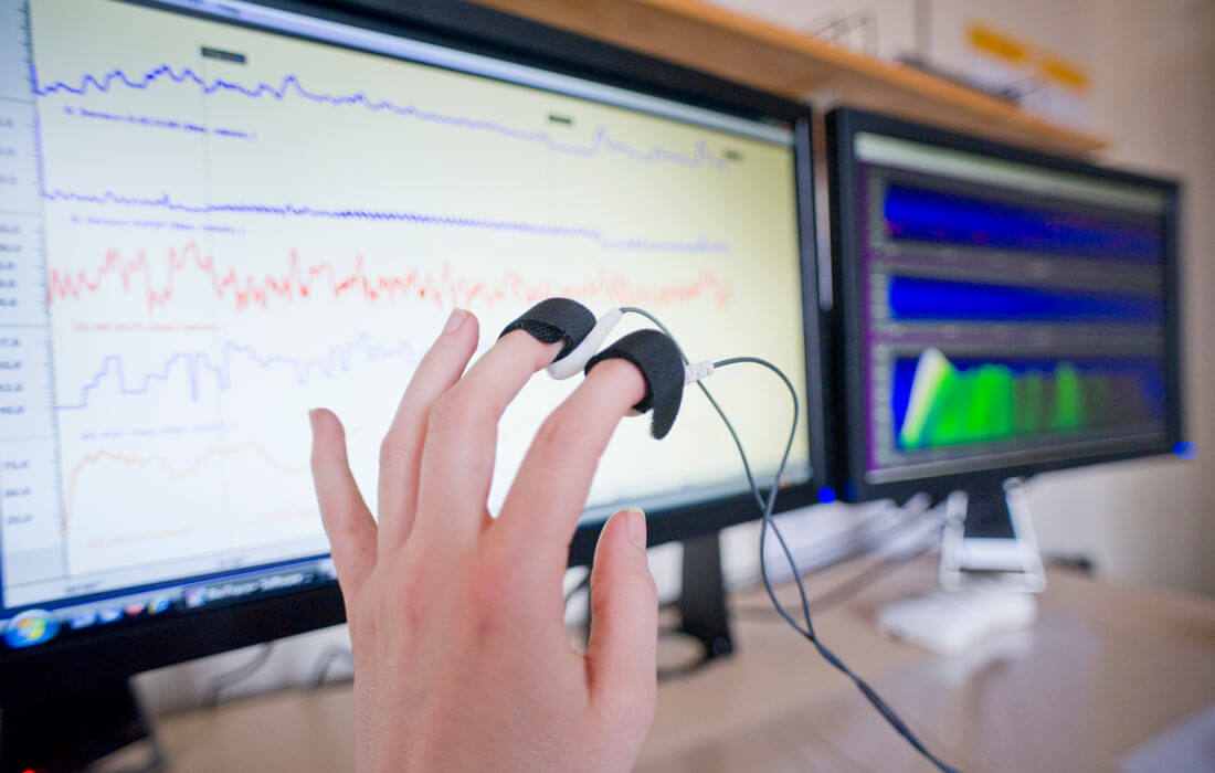 A hand with two sensors attached to it with the readings on screens in the background