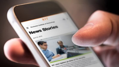 A closeup of a hand holding a phone that shows RIT's research news